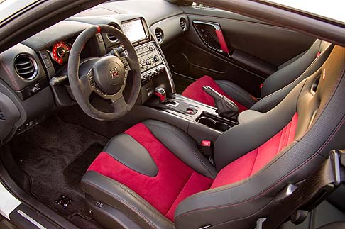 Nissan - Il volante rivestito in Alcantara, presenta tre razze, un contrassegno centrale di colore rosso e giunzioni rosse.  width=